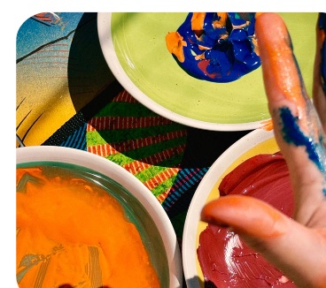 Mains plongées dans des bols de peinture orange, verte et rouge